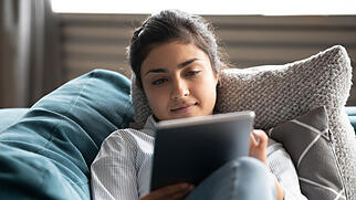 Young indian woman rest on sofa watching movie on tablet